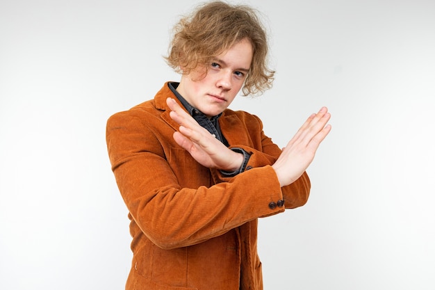 Confident curly blond guy in a brown jacket waves his hands away on a white studio background.