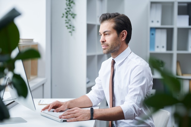 Confident director of business organization sitting in his office in front of computer monitor