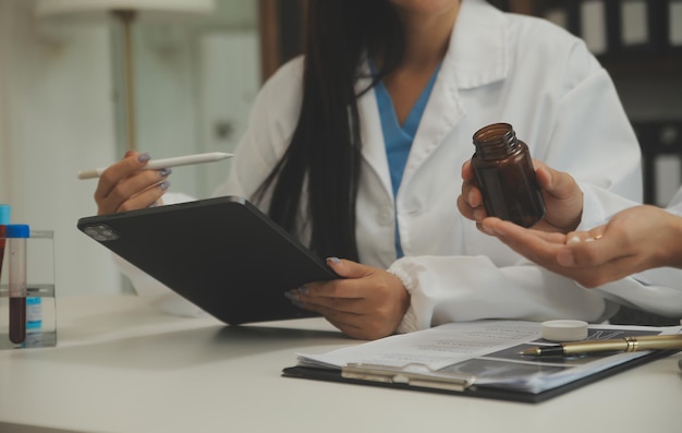 Фото Уверенный в себе врач мужчина держит бутылку с таблетками и пишет, разговаривая со старшим пациентом и просматривая свои лекарства в кабинете