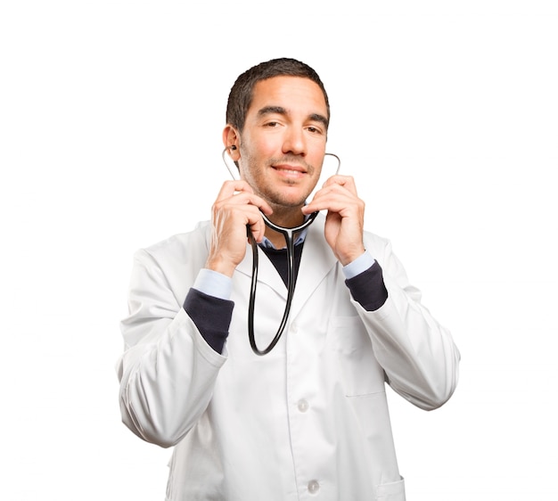 Confident doctor using a stethoscope against white background