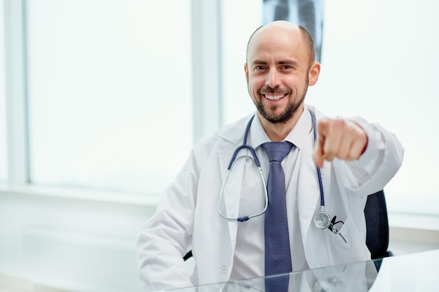 Confident doctor in a white coat pointing at you