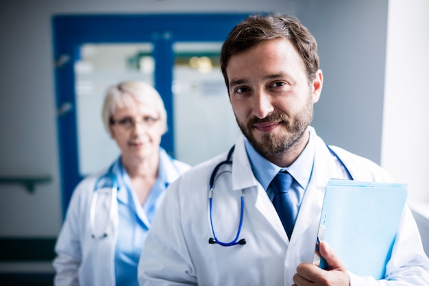 Confident doctor with clipboard standing in hospital corridor