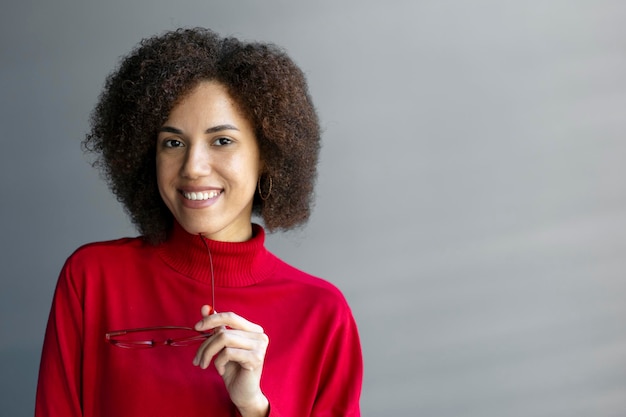 Confident elegant African American pretty woman holding eyeglasses smiles cutely looking at camera