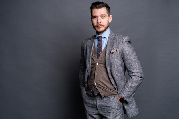 A confident elegant handsome young man standing in front of a grey background in a studio wearing a nice suit.