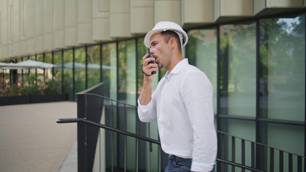 Foto ingegnere sicuro che parla walkietalkie che cammina vicino al distretto uomo che lavora