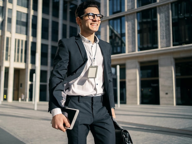 A confident entrepreneur is a young man in glasses and a business suit with a briefcase