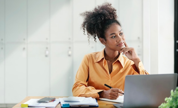 Confident ethnic businesswoman using laptop at work thinking and looking away outside