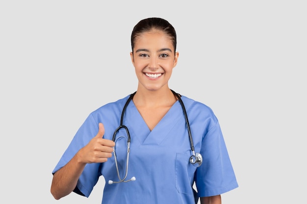 confident european millennial doctor in blue scrubs giving a thumbsup