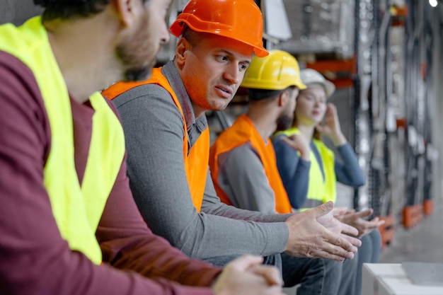 Confident factory foreman worker man wearing hard hat and work wear talking to colleagues