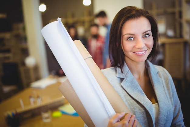 Confident female architect with blueprints in office