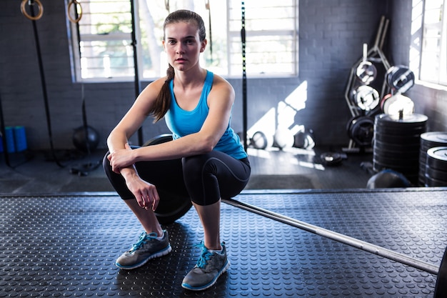 Confident female athlete sitting on barbell