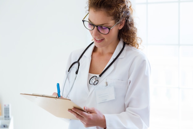 Foto informazioni di scrittura di medico femminile sicuro del suo paziente nell'ufficio.