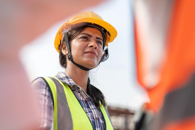 Confident female Indian engineer wearing protective helmet and vest working in construction site