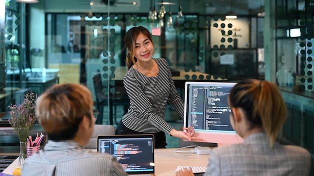 Capogruppo femminile sicuro e giovani ingegneri del software che lavorano con il codice di programmazione sullo schermo del computer in un ufficio contemporaneo