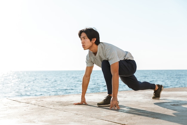 Уверенно подтянутый азиатский спортсмен, тренирующийся на открытом воздухе на берегу моря