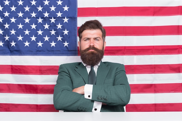 Confident in future of his country. Confident american keep arms crossed. Confident look of serious businessman. Independence day. July 4th. USA flag background. Proud and confident.