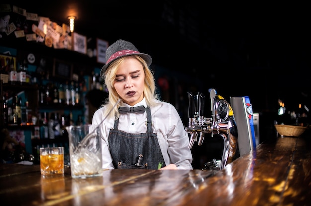 Confident girl bartender pouring fresh alcoholic drink into the glasses at bar