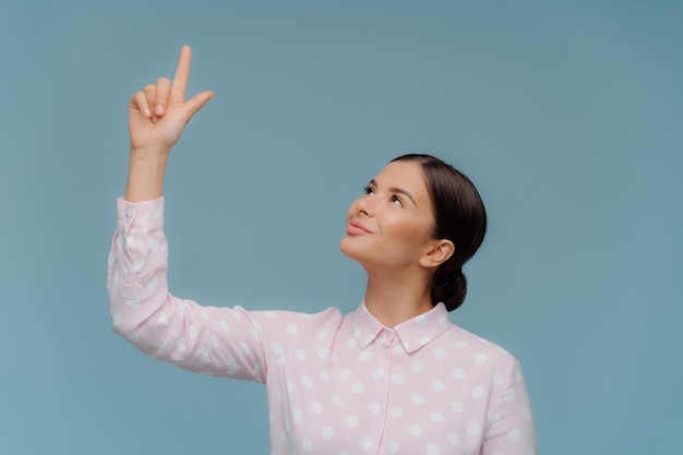 Confident good looking elegant woman points above on free space