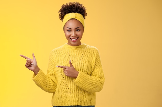 Confident good-looking millennial feminine african-american woman headband sweater look self-assured assertive pointing left index fingers you gonna like it smile, standing yellow background.