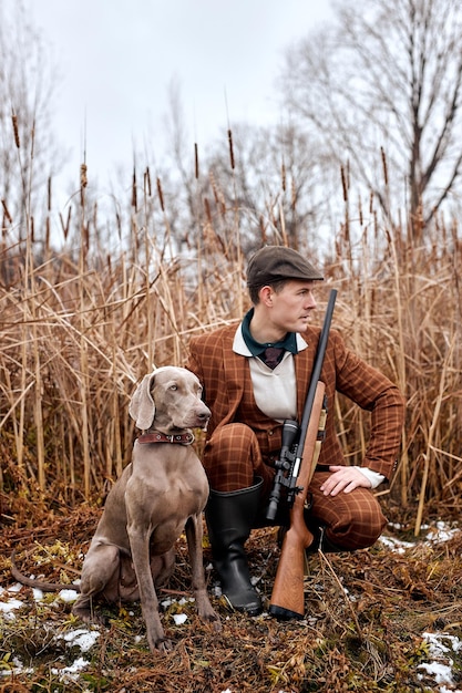 Confident guy with weimaraner dog sitting in bushes and hunting down an animal in wild nature hunter