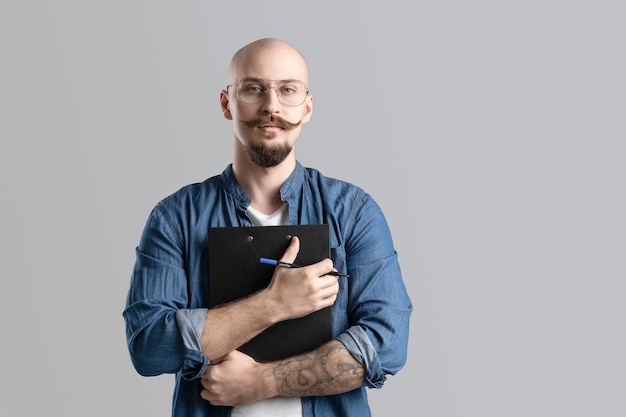 Confident handsome balded beard with musctache man wearing casual clothes holding clipboard isolated