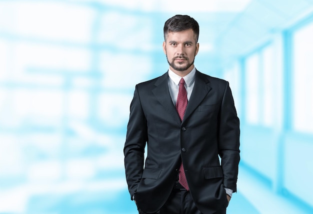 Confident handsome businessman with arms in pockets on background