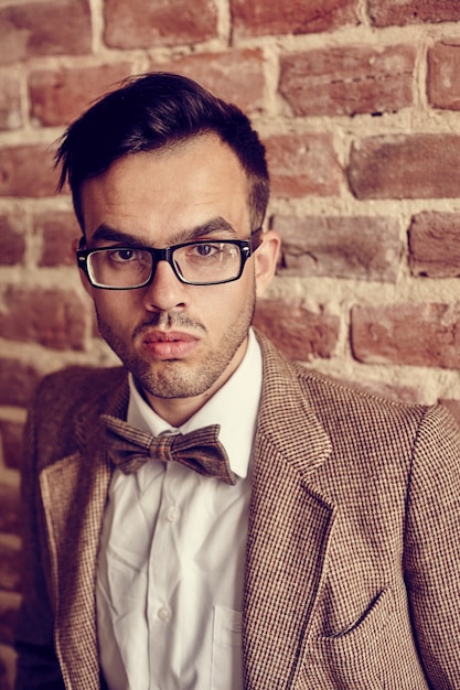 Confident handsome young  man standing with his hands in his pocket against a brick surface