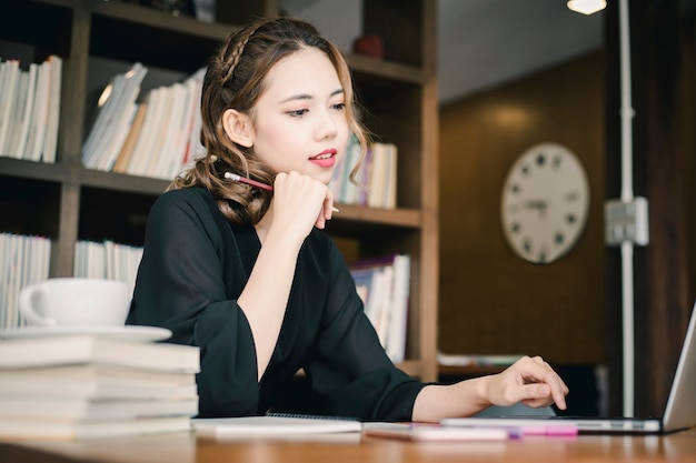 自信を持って幸せ若い女性は彼女のオフィスでラップトップやノートブックで働いています。