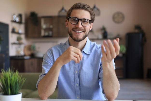 Confident happy businessman in eyeglasses sitting at home\
workplace and looking at camera.