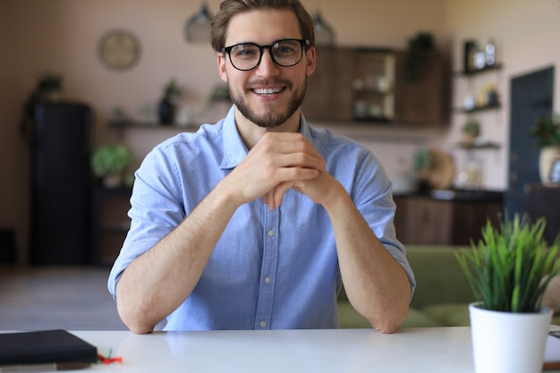 Confident happy businessman in eyeglasses sitting at home workplace and looking at camera.