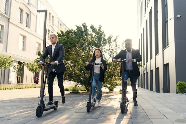 Confident happy multiracial office colleagues discussing business project go near office building with electric scooters