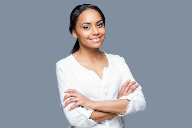 Confident in her beauty. Portrait of attractive young African woman keeping arms crossed and smiling while standing against grey background