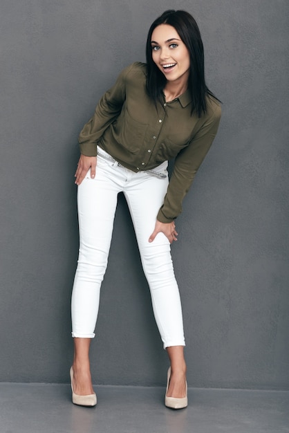 Confident in her perfect look. Full length of happy young woman in smart casual wear standing against grey background and looking at camera