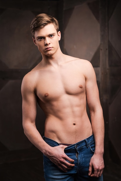 Confident in his perfect body. Handsome young muscular man posing while standing against metal background