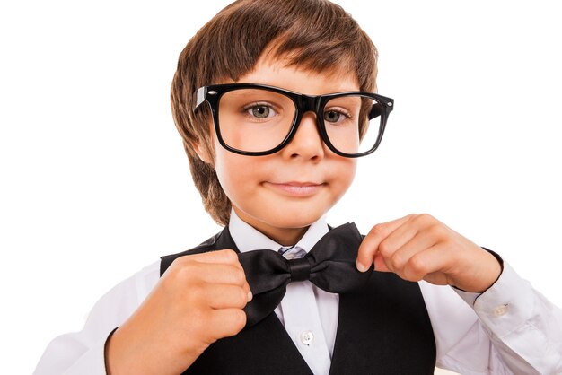 Confident in his skills. Cute little boy adjusting his bow tie and looking at camera while standing isolated on white