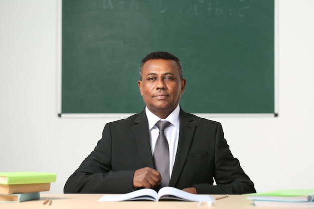 Confident Indian teacher sitting at table in classroom