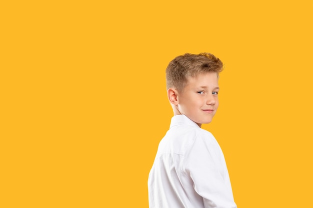 Confident kid portrait. Schoolboy lifestyle. Cheerful boy looking over shoulder isolated on orange copy space.