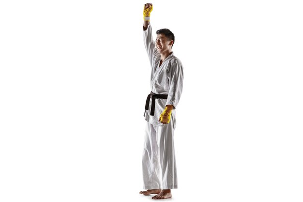 Confident korean man in kimono practicing hand-to-hand combat, martial arts. Young male fighter with black belt celebrates win isolated on white studio background. Concept of healthy lifestyle, sport.