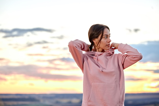 Confident lady is preparing for training outdoors, looking at side in contemplation, getting ready for jogging, in pink sportive hoodie. active woman is motivated and concentrated on sport