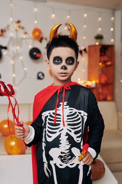 Foto fiducioso ragazzino vestito da diavolo che tiene il tridente e cerca halloween