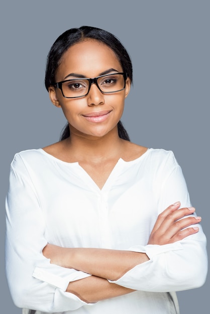 Confident look. Attractive young African woman adjusting her eyeglasses and looking at camera while standing against grey background