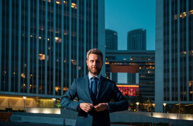 Photo confident male manager outdoor near modern office night building business man stand up and night city background
