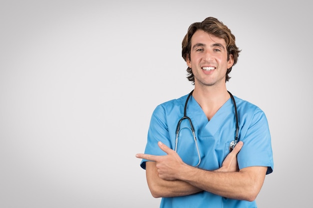 Confident male nurse in blue scrubs pointing sideways at free space with smile