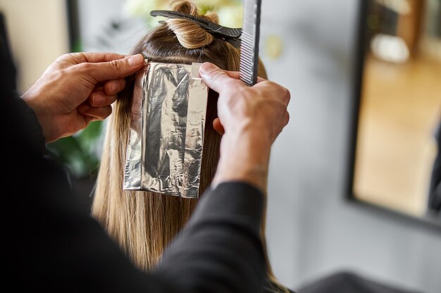 Photo confident male stylist is dyeing hair of blond caucasian female client