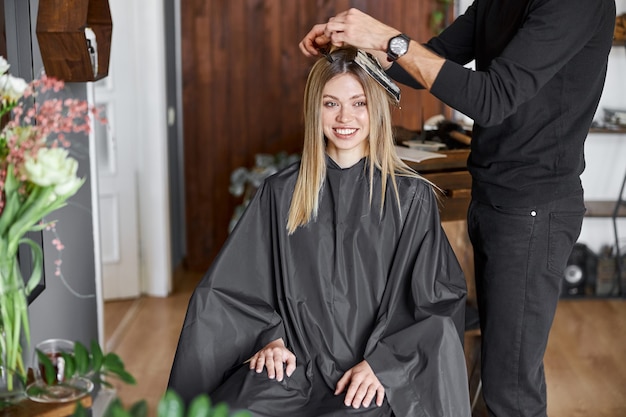 Confident male stylist is dyeing hair of blond caucasian female client