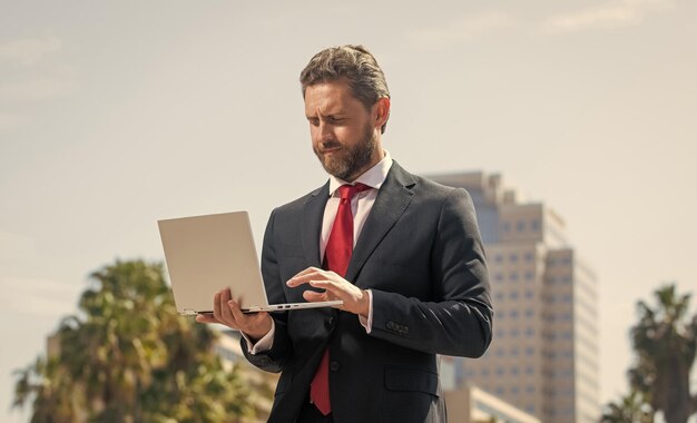 Confident man in elegant suit checking email on pc outside\
agile business