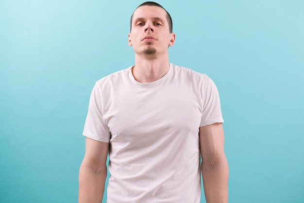 A confident man looks at the camera and holds his head raised on a blue background Modern One Studio White Young Casual Fashion Lifestyle Authority Concentration Hold Isolated