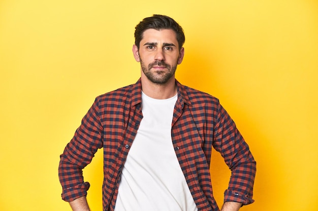 Confident man in red plaid shirt on a yellow studio background