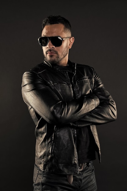 Confident man stand with arms folded bearded man in trendy
sunglasses fashion model in leather jacket and jeans fashion and
style confidence with sexuality and charisma