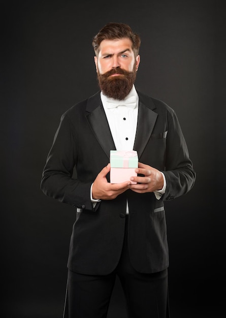 Уверенный в себе мужчина в формальной одежде смокинг с галстуком-бабочкой на черном фоне с коробкой на мужской день